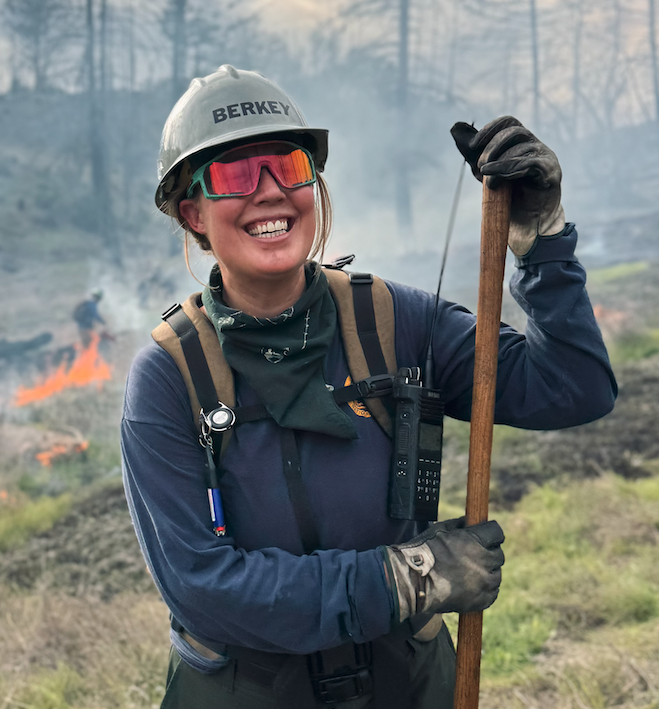 a prescribed fire tender stands in forested area with flames in background