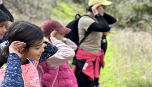 two young girls and a hike leader place their hands behind their ears to listen for wildlife