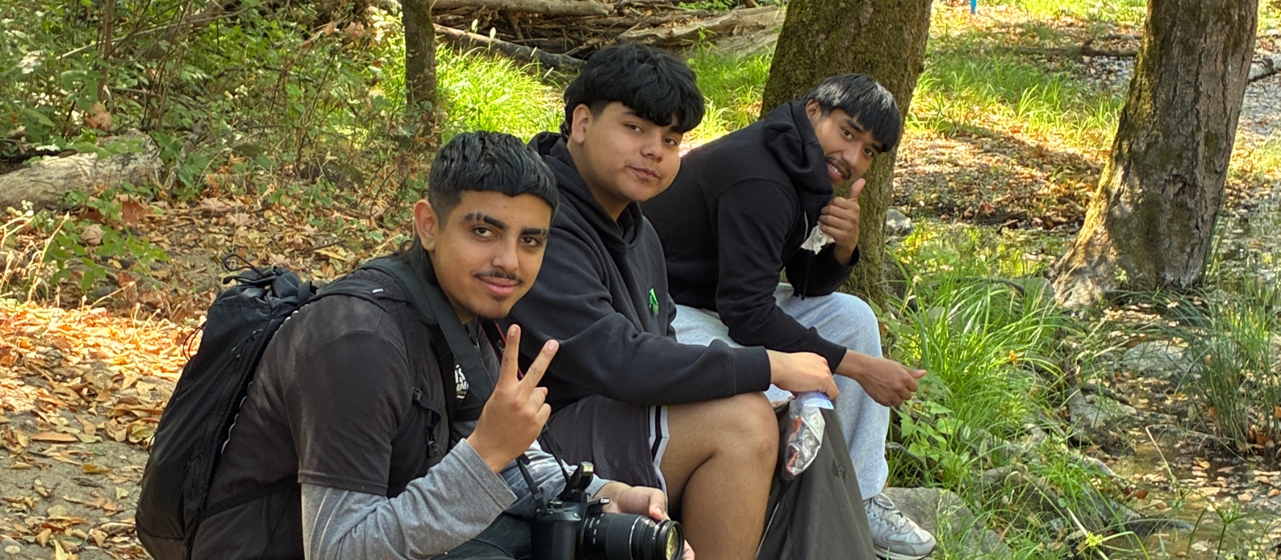 Three young men seated next to one another in nature face the camera