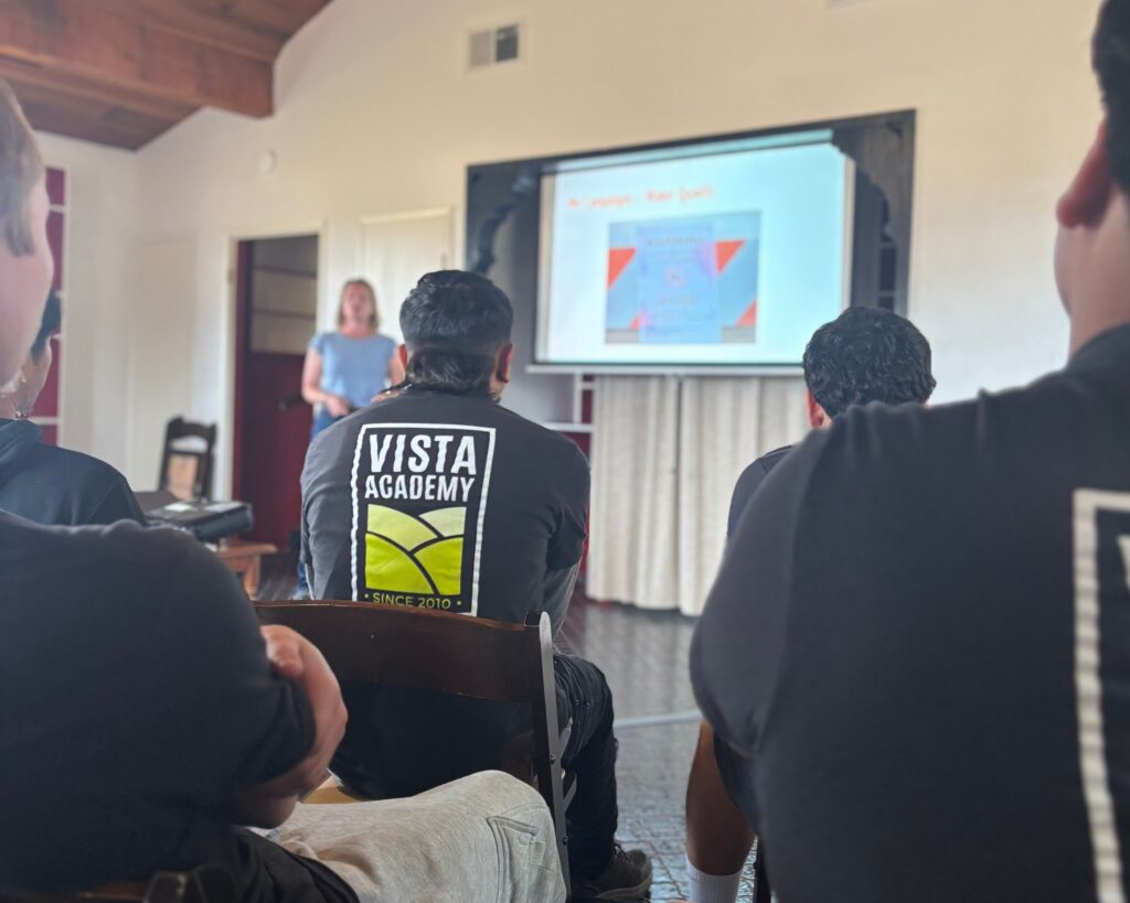 The backs of youth taking a class. the words Vista Academy of a shirt.