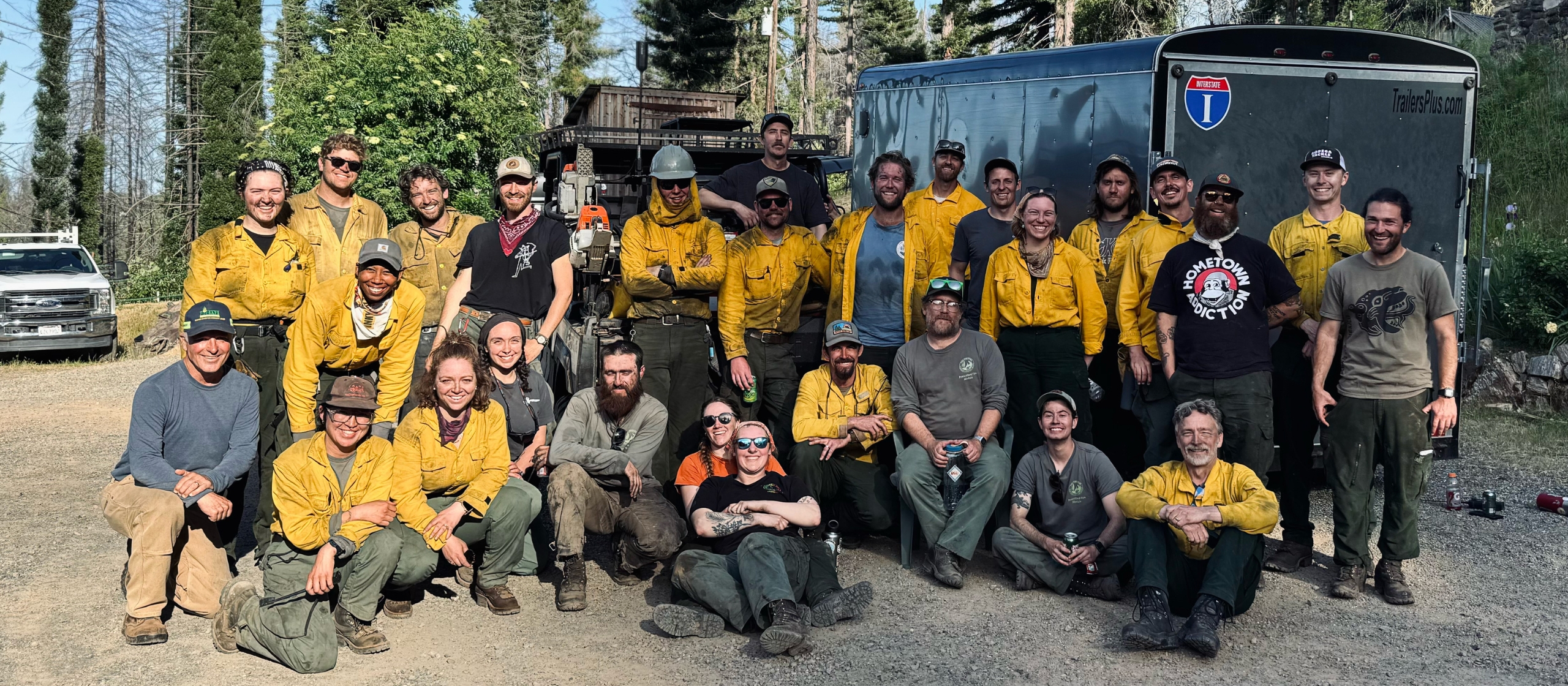 A group of workers, many in yellow shirts, looking sweaty and with ash soot on them are smiling as they stand in three lines facing the camera.
