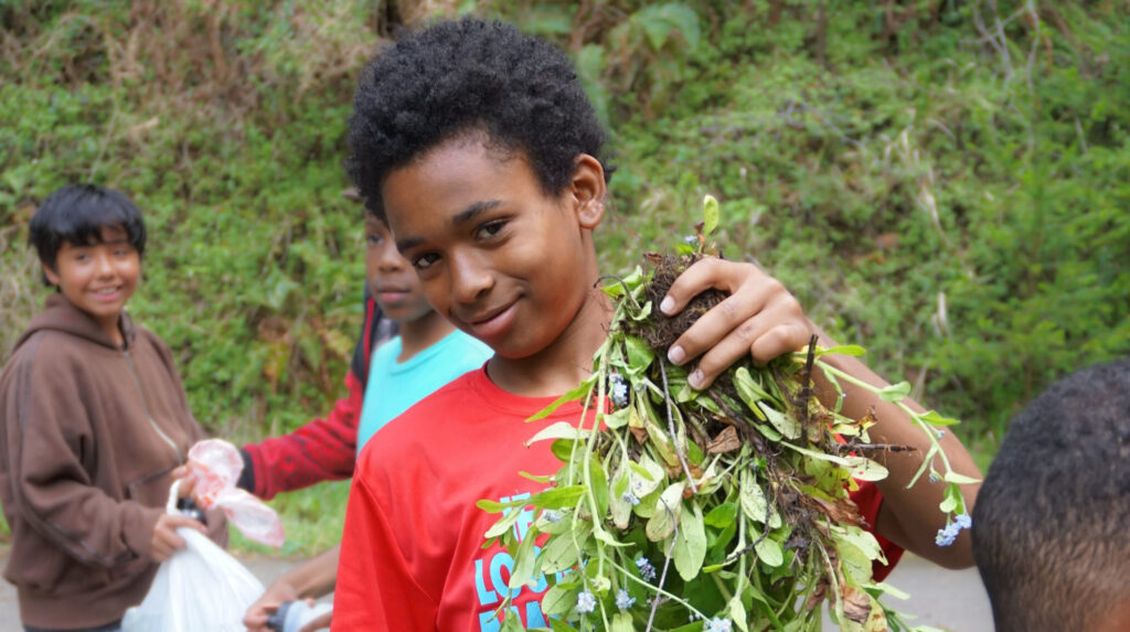 An adolescent boy holds up a weed by the roots smiling.