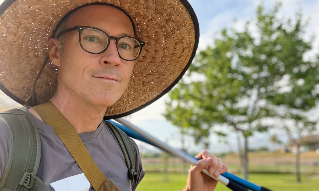 A man in a sunhat and glasses with a green tree in the background. 
