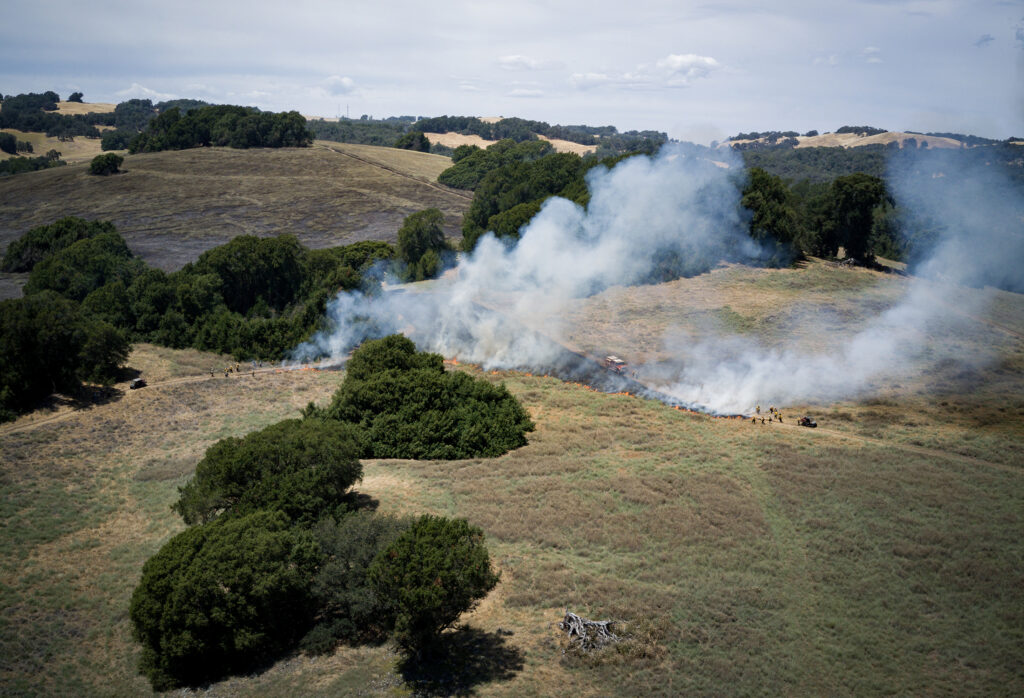 An aerial shot of a prescribed fire in a dry field with smoke lifting in the breeze.